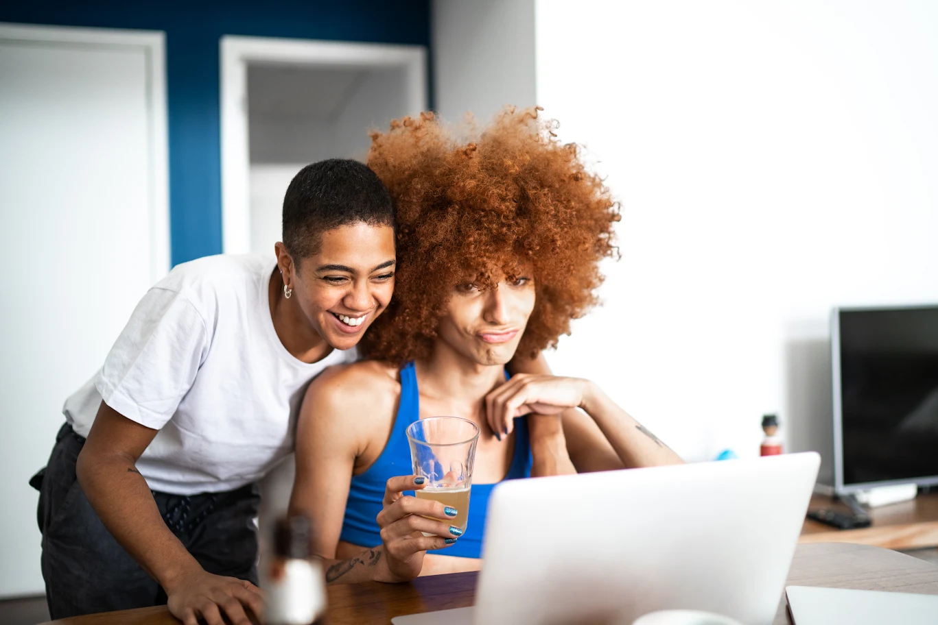 Two friends smiling while looking at a laptop screen.